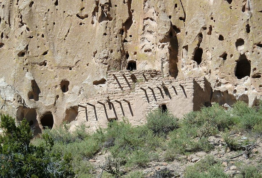 A panoramic view of Bandelier National Monument, showcasing ancient Puebloan cliff dwellings carved into the rocky cliffs. The site is rich in history, featuring petroglyphs and artifacts from the ancestral Pueblo people. The rugged terrain and scenic trails provide opportunities for exploration and appreciation of the stunning natural beauty."